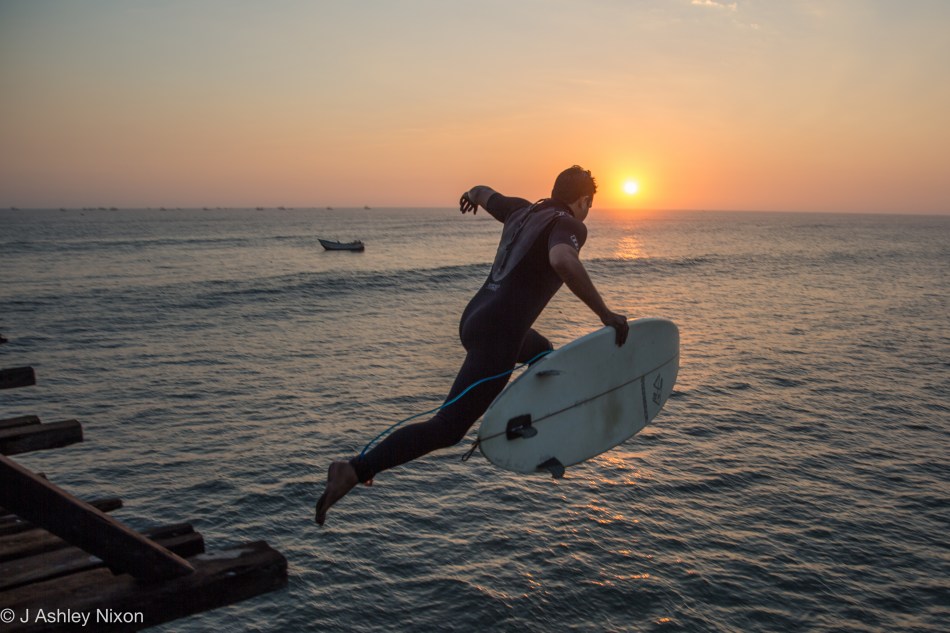 Alonso, a local surfer, jumps off the pier at Pimentel, Peru into the sun and the Pacific Ocean. Aug 25, 2016. © J. Ashley Nixon